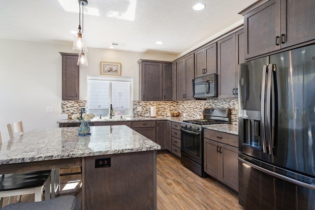 kitchen featuring light stone counters, stainless steel appliances, light wood-style floors, dark brown cabinets, and a sink