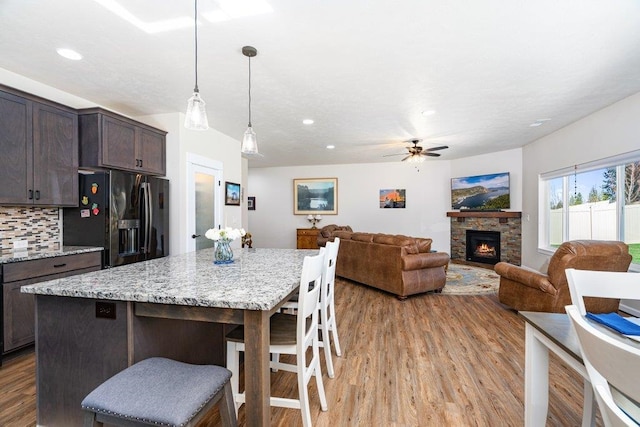 kitchen with black fridge with ice dispenser, a breakfast bar, light wood-style floors, ceiling fan, and dark brown cabinets