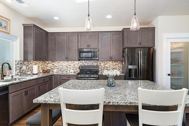 kitchen featuring a sink, appliances with stainless steel finishes, visible vents, dark brown cabinets, and a kitchen island
