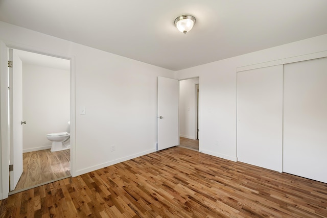 unfurnished bedroom with connected bathroom, a closet, wood finished floors, and baseboards