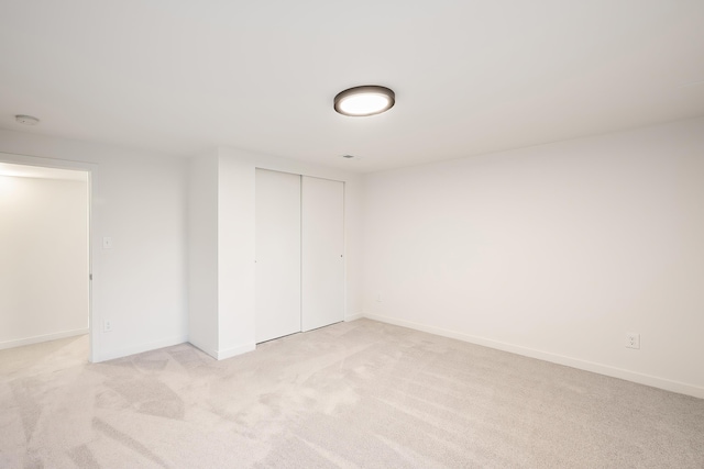 unfurnished bedroom with a closet, light colored carpet, and baseboards