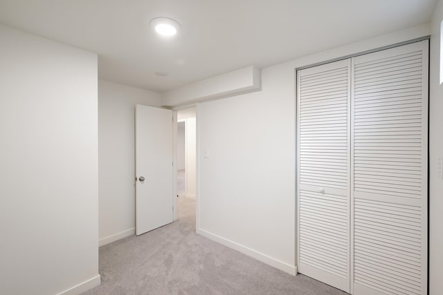 unfurnished bedroom with a closet, light colored carpet, and baseboards
