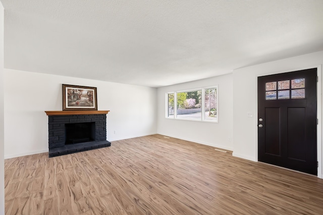 unfurnished living room featuring a textured ceiling, a fireplace with raised hearth, light wood finished floors, and baseboards