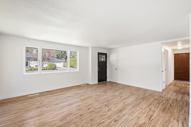 unfurnished living room with baseboards, a textured ceiling, and light wood finished floors