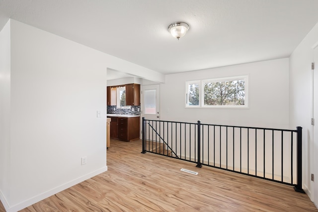 empty room with visible vents, light wood-type flooring, and baseboards