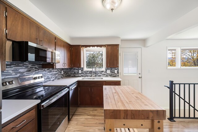 kitchen featuring backsplash, appliances with stainless steel finishes, light wood-style flooring, and a sink