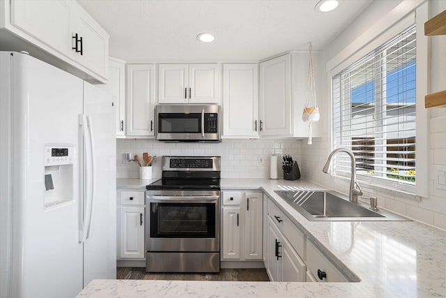 kitchen with light stone countertops, decorative backsplash, appliances with stainless steel finishes, white cabinets, and a sink