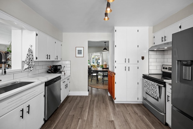 kitchen with dark wood-style flooring, stainless steel appliances, decorative backsplash, and under cabinet range hood