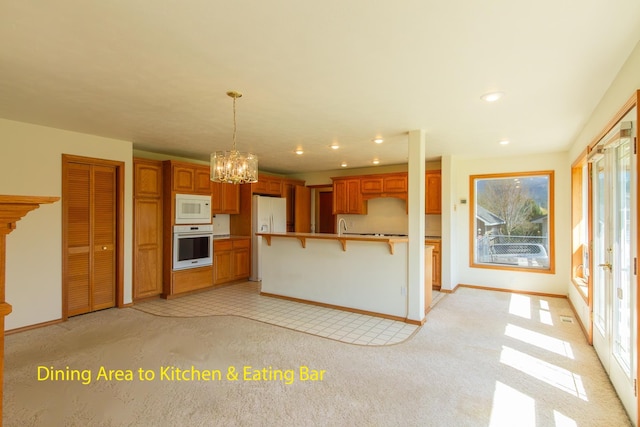 kitchen featuring a kitchen breakfast bar, light colored carpet, white appliances, a notable chandelier, and brown cabinetry