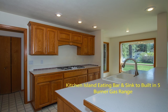 kitchen with recessed lighting, a sink, white gas stovetop, brown cabinetry, and light countertops
