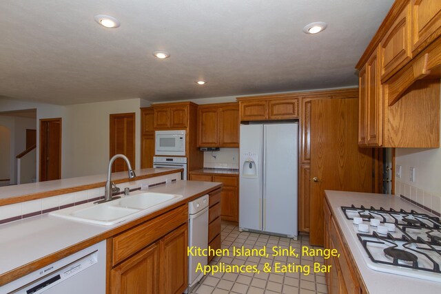 kitchen featuring white appliances, light tile patterned floors, light countertops, brown cabinets, and a sink