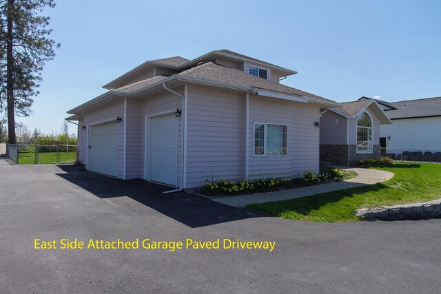 view of home's exterior featuring roof with shingles, an attached garage, aphalt driveway, and fence
