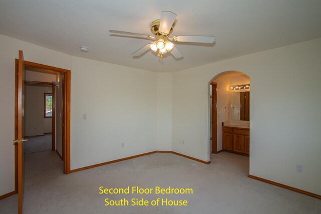 unfurnished bedroom featuring arched walkways, a ceiling fan, light colored carpet, and baseboards