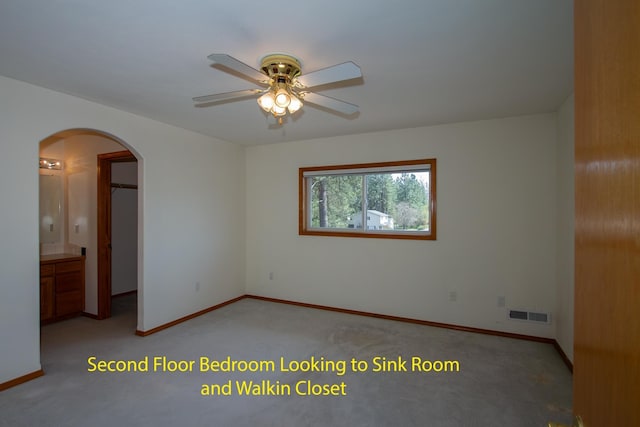 unfurnished room with visible vents, arched walkways, a ceiling fan, and light colored carpet