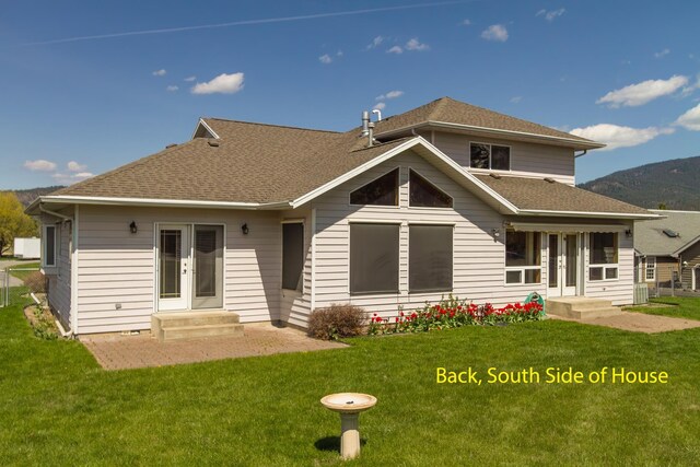 rear view of property featuring a shingled roof and a lawn