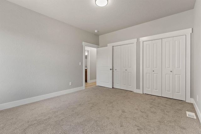 unfurnished bedroom with carpet, two closets, and baseboards
