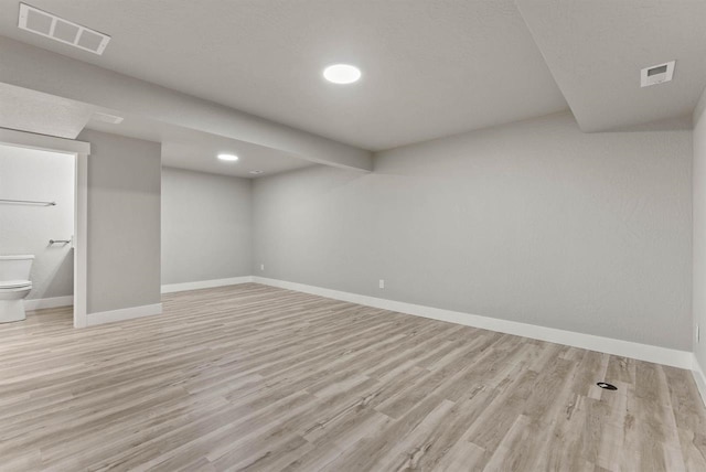finished below grade area featuring visible vents, light wood-style floors, and baseboards