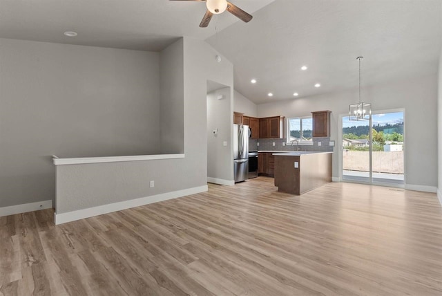 kitchen featuring freestanding refrigerator, light countertops, vaulted ceiling, ceiling fan with notable chandelier, and open floor plan