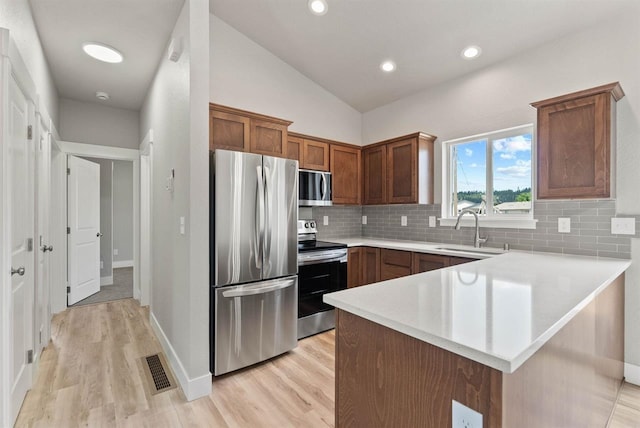 kitchen featuring light wood-style floors, a peninsula, appliances with stainless steel finishes, and a sink