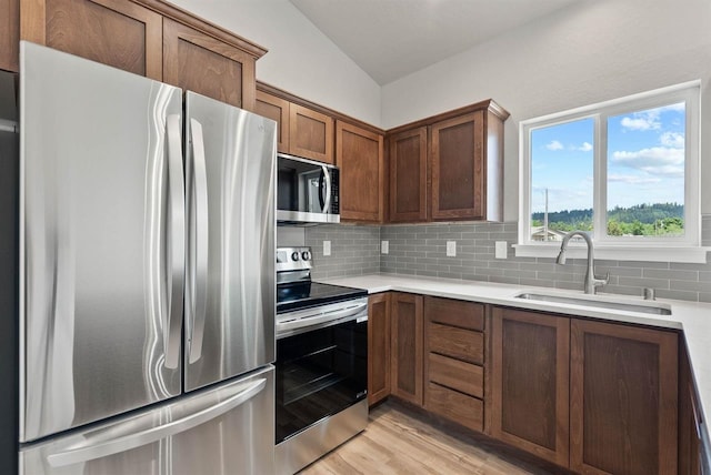 kitchen with a sink, decorative backsplash, light wood-style floors, light countertops, and appliances with stainless steel finishes