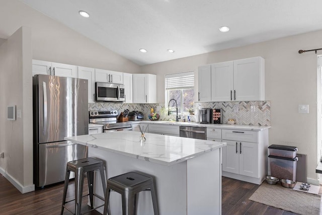 kitchen with dark wood finished floors, a breakfast bar, appliances with stainless steel finishes, a kitchen island, and white cabinets