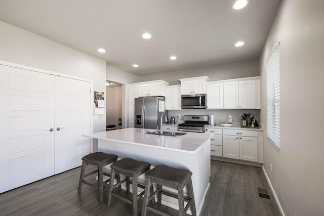 kitchen with a kitchen island with sink, stainless steel appliances, a sink, white cabinetry, and a kitchen breakfast bar