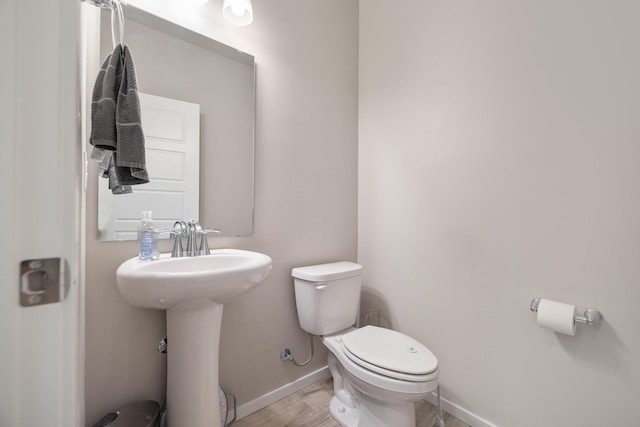 half bathroom featuring baseboards, wood finished floors, toilet, and a sink