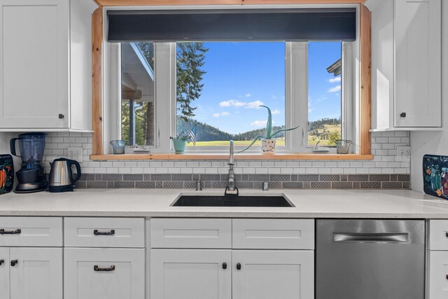 kitchen with white cabinetry, stainless steel dishwasher, a sink, light countertops, and backsplash