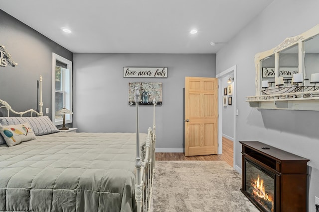 bedroom featuring recessed lighting, baseboards, wood finished floors, and a glass covered fireplace