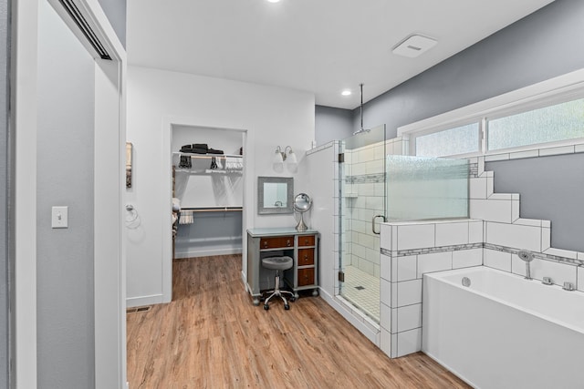 full bathroom with a bath, a walk in closet, a shower stall, and wood finished floors