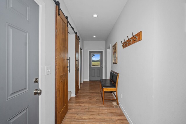hallway featuring recessed lighting, a barn door, light wood-type flooring, visible vents, and baseboards