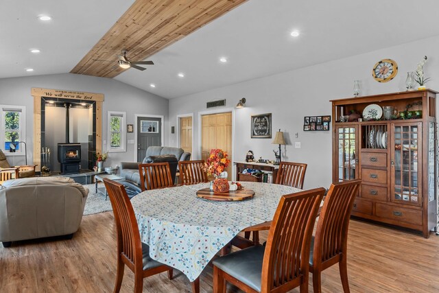 dining space with a wood stove, recessed lighting, light wood-style floors, a ceiling fan, and lofted ceiling