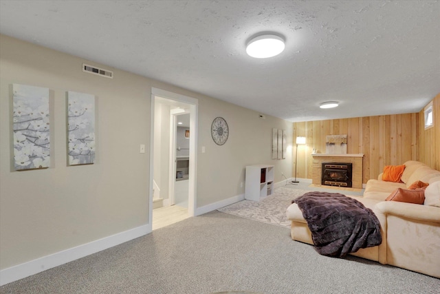 living area with carpet floors, wood walls, a fireplace, visible vents, and a textured ceiling