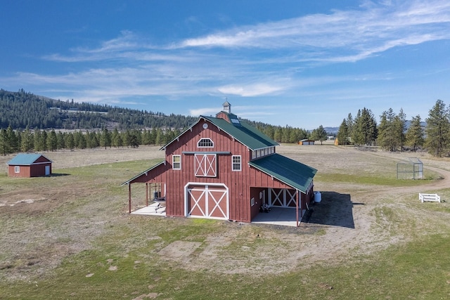 view of barn with a lawn, driveway, and a forest view