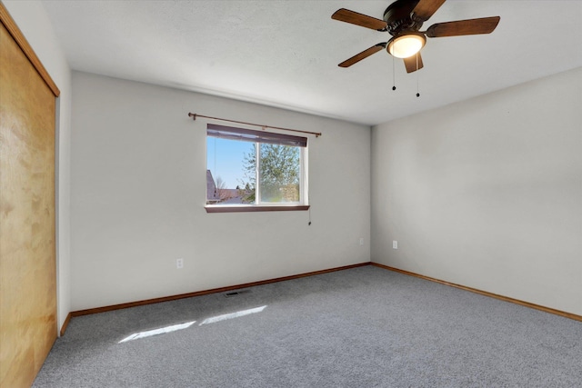 carpeted spare room featuring visible vents, ceiling fan, and baseboards