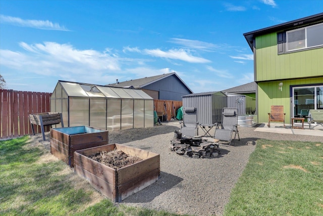 view of patio featuring an outdoor structure, a greenhouse, a storage unit, an outdoor fire pit, and a fenced backyard