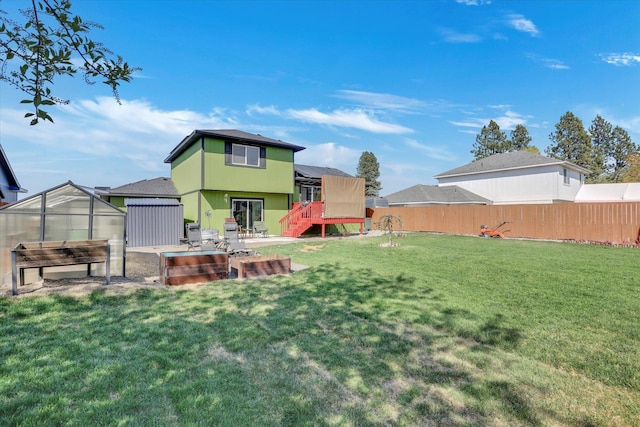 rear view of property featuring a patio area, an outbuilding, a greenhouse, a yard, and a fenced backyard