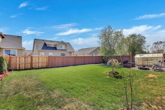 view of yard featuring a fenced backyard, a greenhouse, and an outbuilding