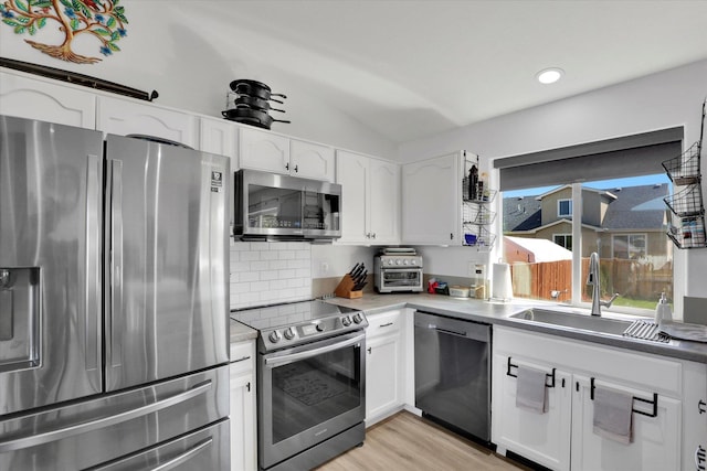 kitchen featuring appliances with stainless steel finishes, white cabinetry, vaulted ceiling, and a sink
