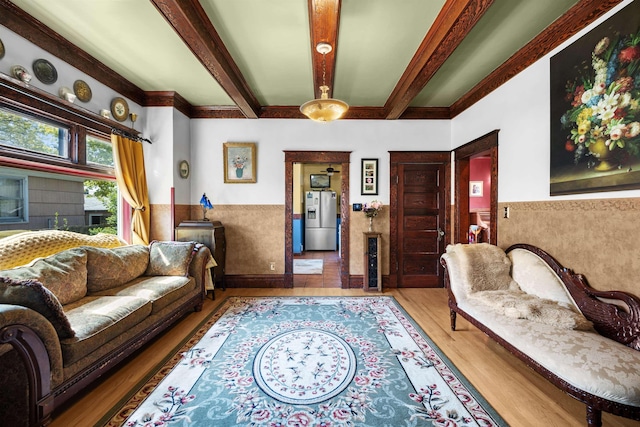 living area featuring beamed ceiling, wainscoting, and wood finished floors