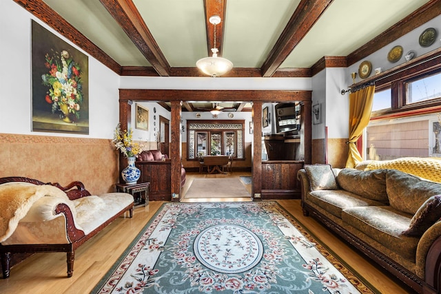 living room featuring beam ceiling, a wealth of natural light, wood finished floors, and wainscoting