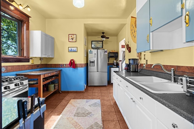 kitchen featuring white cabinets, a sink, ceiling fan, dark countertops, and stainless steel appliances