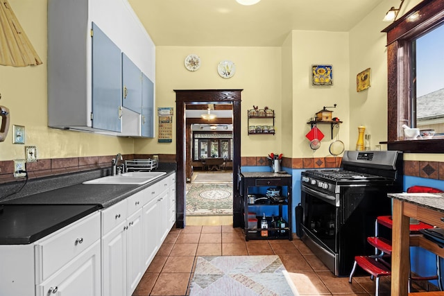 kitchen with stainless steel range with gas cooktop, white cabinetry, a sink, dark countertops, and dark tile patterned floors