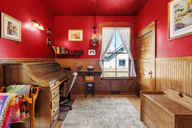office area featuring wood walls, wood finished floors, visible vents, and wainscoting