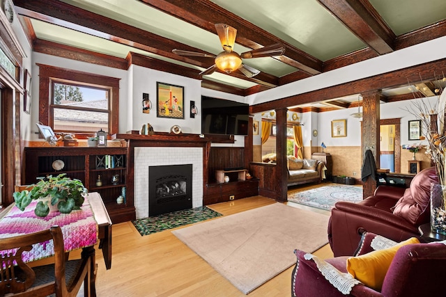 living room featuring a tile fireplace, beam ceiling, ceiling fan, ornate columns, and wood finished floors