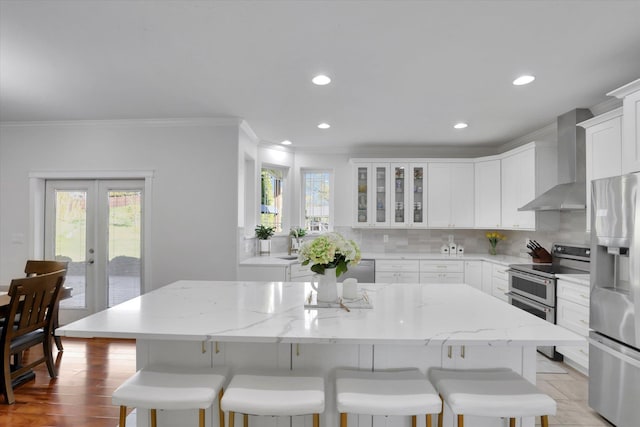 kitchen with a breakfast bar area, crown molding, appliances with stainless steel finishes, wall chimney exhaust hood, and backsplash