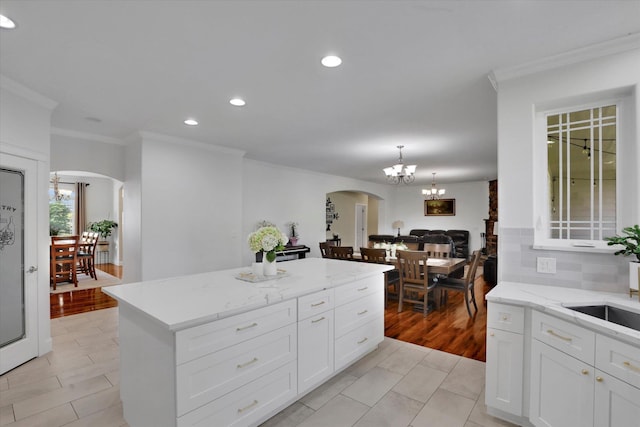 kitchen with arched walkways, an inviting chandelier, ornamental molding, and a kitchen island