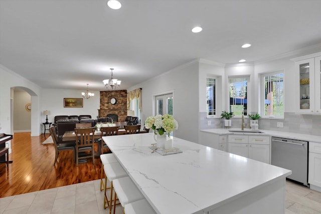 kitchen with arched walkways, stainless steel dishwasher, crown molding, and a sink