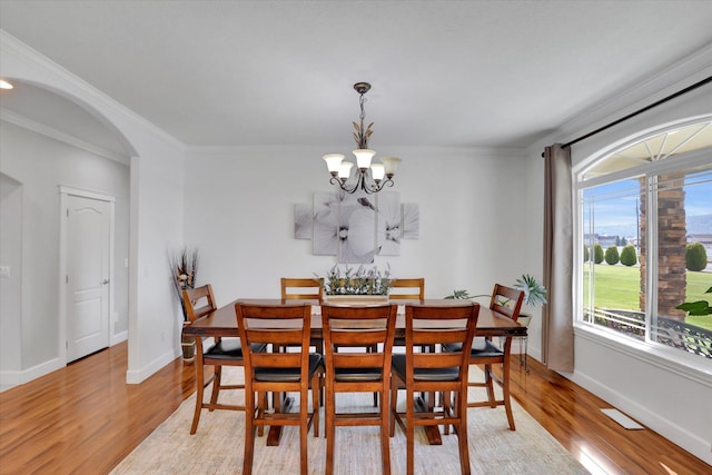 dining room featuring light wood finished floors, arched walkways, a chandelier, and baseboards