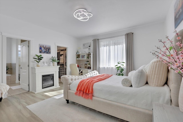 bedroom with light wood-style flooring, a closet, ensuite bathroom, a glass covered fireplace, and a spacious closet